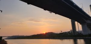 Campsites and riverside parkland along the Ara Waterway at sunset, seen from beneath the bridge