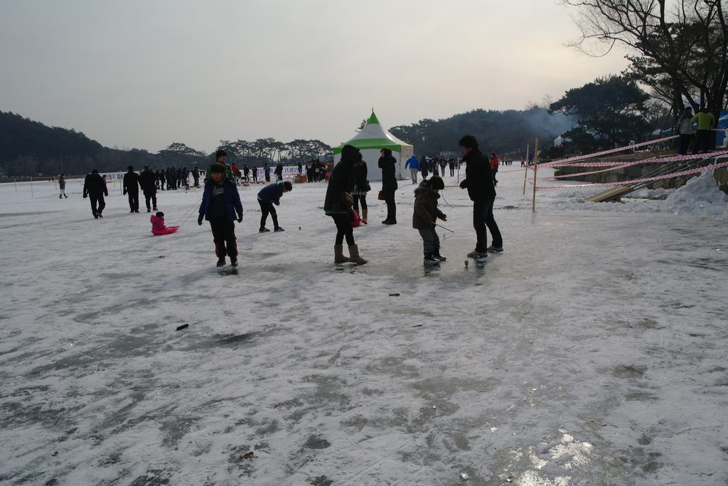 Children trying traditional top spinning at an organized winter festival on a frozen reservoir