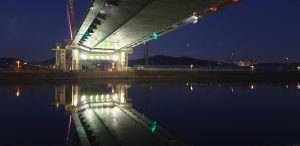 The underside of Gyeyang Bridge lit up at night, reflected in the calm canal water