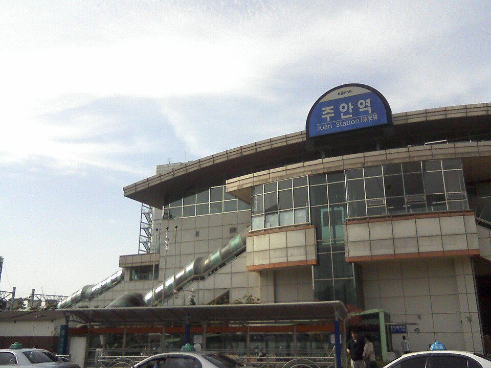 Curved glass and concrete station building with a rounded blue sign reading Juan Station in Korean and English above the entrance