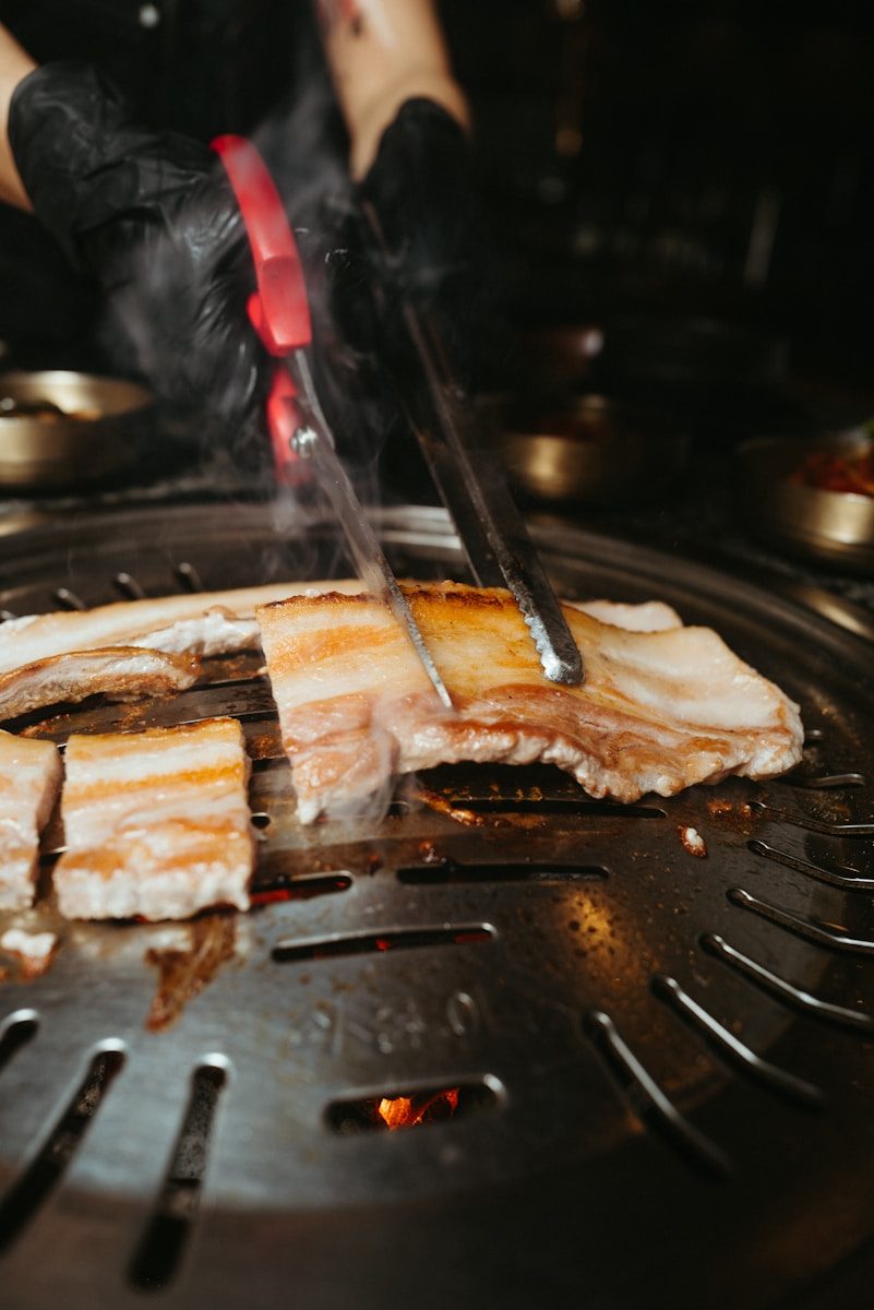 Samgyeopsal pork belly grilling on a tabletop grill with Korean side dishes