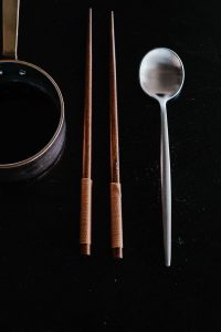 A pair of metal chopsticks and a long-handled spoon resting on a table