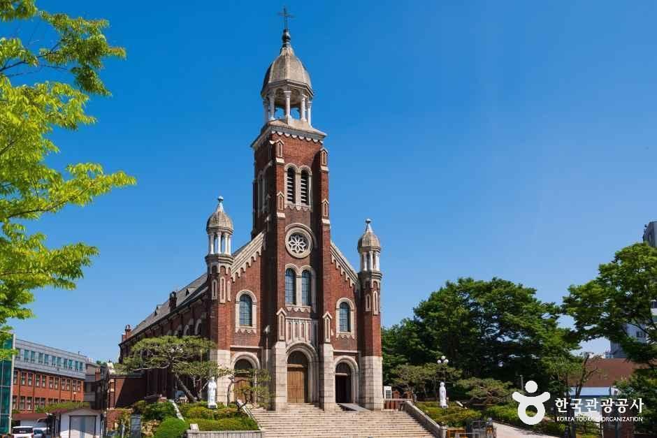 Red brick church with a domed bell tower and rose window seen from the front steps under a clear blue sky