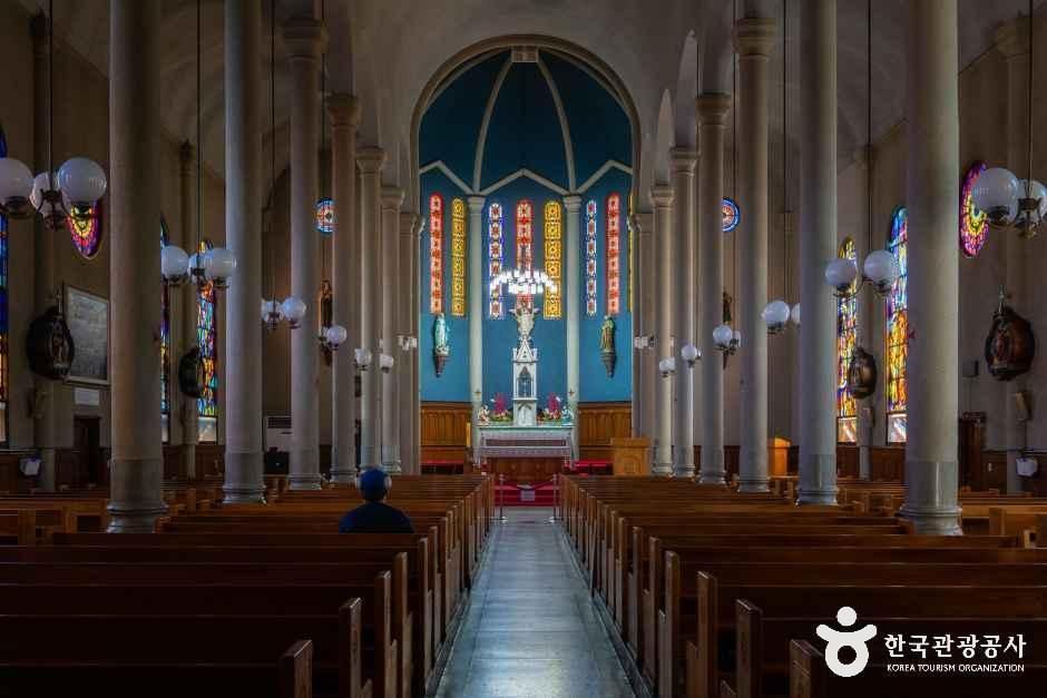 Church interior with rows of wooden pews, white columns, and stained glass windows along both walls