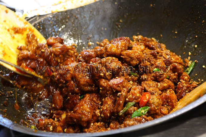 Glazed fried chicken pieces being tossed in a large wok with peppers