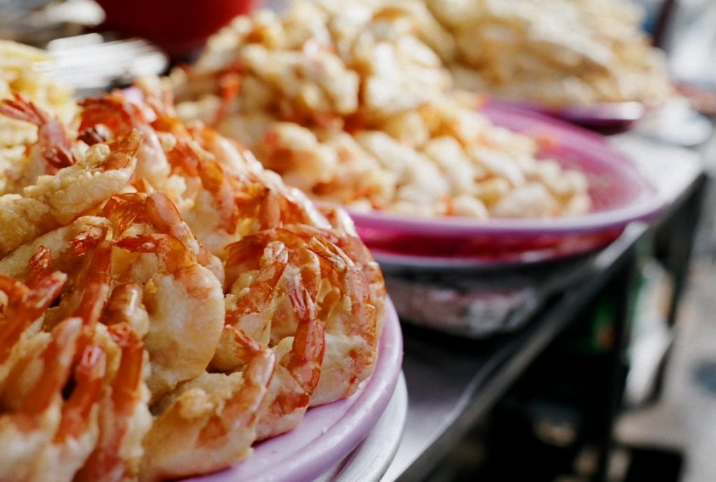 Plates of battered fried shrimp stacked on a market stall counter