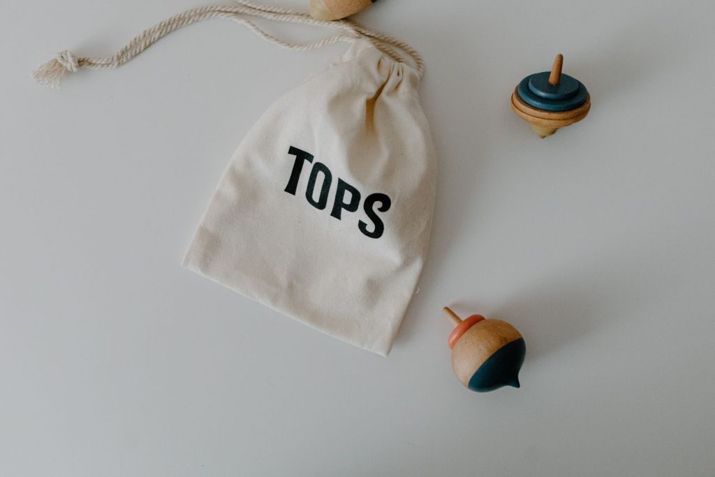 Wooden spinning tops with a string bag reading 'Tops' on a white background.