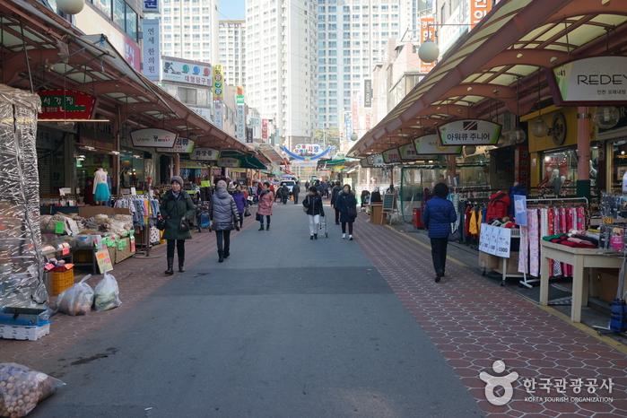 Covered main street of Moraenae Market in Incheon with shoppers walking and high-rise apartments rising behind the market
