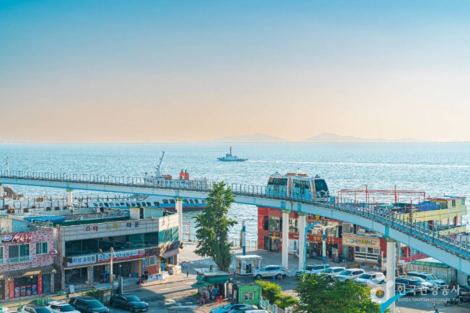 Elevated monorail train passing above shops and restaurants beside the sea