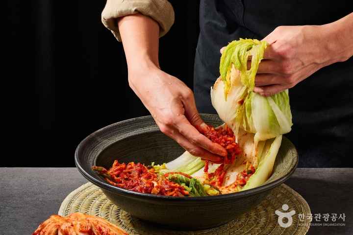 Spicy kimchi seasoning is being spread over salted napa cabbage leaves.